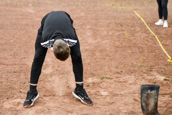 A teenager in sportswear throws a rubber boot on an ash track rubber boots long throw sports and fun Olympics sports festival school, Lower Saxony, Germany