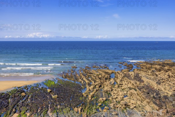 Rocky seashore in low tide with rolling sea waves and a seascape view to the horizon on a sunny summer day, Crozon peninsula, Bretagne, France