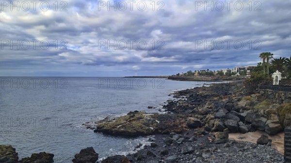 Rocky coast overlooking the sea and urban buildings under a cloudy sky, Playa Blanca Lanzarote