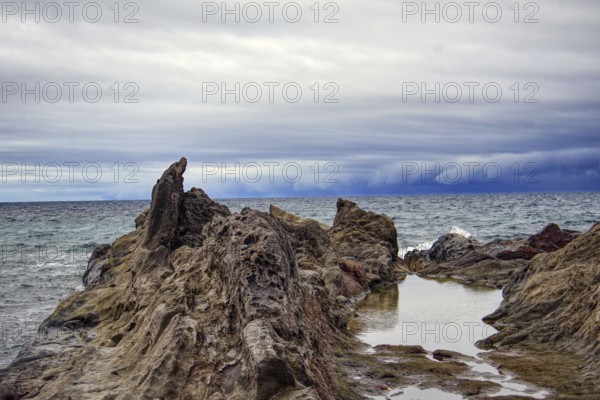 Rugged coastal landscape with rocks in the foreground and a cloudy sky over the sea, Chargo Verde El Golfo Lanzarote