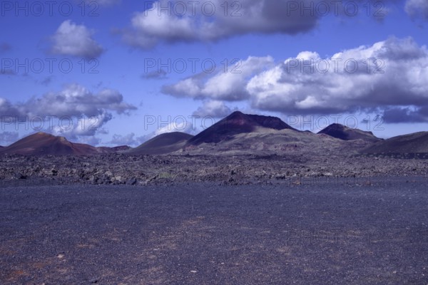 View of a vast volcanic landscape with colorful mountains under a cloudy sky, Tinajo Lanzarote