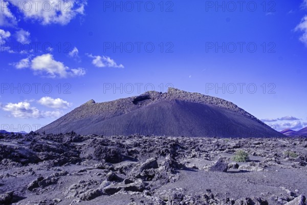 The El Cuervo volcano (Caldera de los Cuervos) rises above a lava field under a clear blue sky, Tinajo Lanzarote