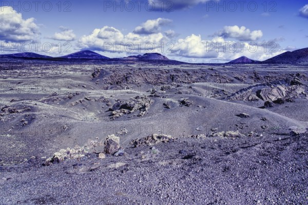 Wide, dry volcanic landscape with rolling hills and mountains under a cloudy blue sky, Tinajo Lanzarote