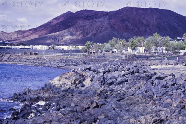 Rugged coastal area with rocks and views of reddish brown mountains under cloudy sky, Playa Blanca Lanzarote