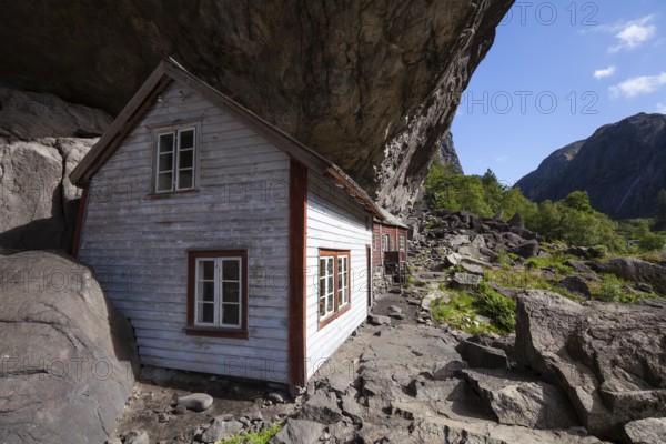 Historical wooden houses sheltered under a massive rock overhang. Summer, Helleren (Helleren), Rogaland, Norway