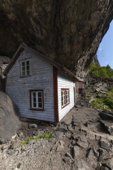 Historical wooden houses sheltered under a massive rock overhang. Summer, Helleren (Helleren), Rogaland, Norway
