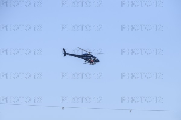 A helicopter flies over a high-voltage line in the air during technical work, Lemförde, Lower Saxony, Germany