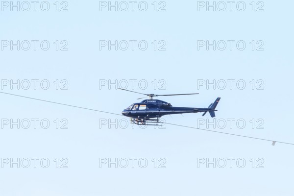 A blue helicopter flies in a clear sky. Technical details are visible, marking work on a new high-voltage line, Lemförde, Lower Saxony, Germany