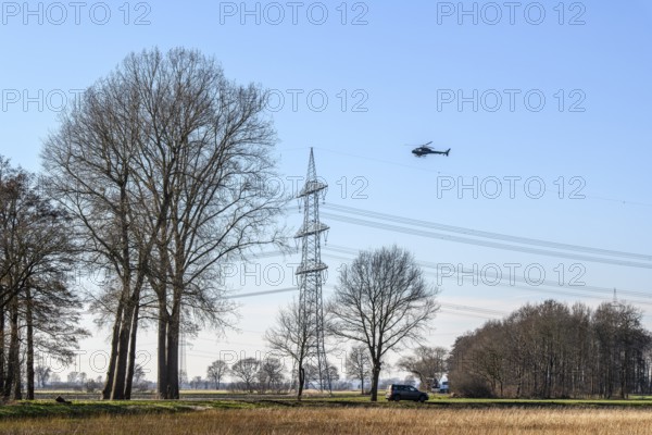 A helicopter flies over a landscape with power poles and trees under a blue sky, Lemförde, Germany, Lower Saxony