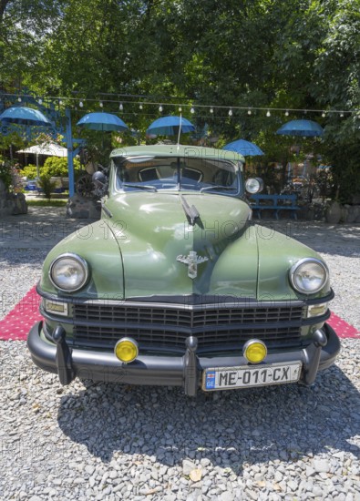 Front view of a green vintage car on a red carpet surrounded by umbrellas and pebbles, vintage car, Chrysler Windsor limousine, Georgia