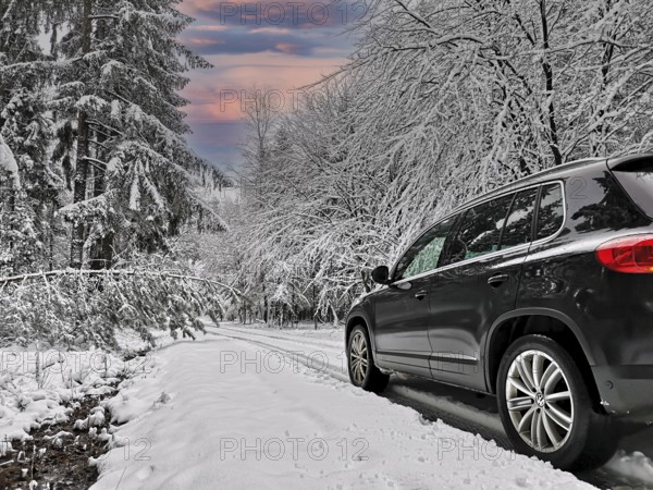 Black SUV driving on deep snowy road through winter forest, Baden-Württemberg, Germany
