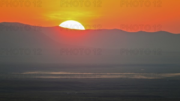 Sunrise with red fireball of rising sun over mountain ridges and extensive steppe landscape in the lowlands of a river with yurts and horses, Bulgan, Mongolia