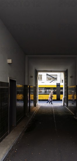 View through a corridor to the backyard onto Chässeestraße with passengers and moving tram, Berlin, Germany