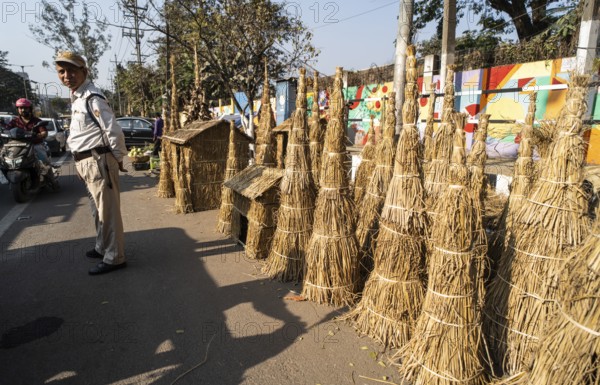 A police personnel stands as vendor display Meji (Bonfire) to sell near a road, as part of preparations ahead of the 'Magh Bihu' festival, in Guwahati, Assam, India on January 12, 2026. Magh Bihu, also called Bhogali Bihu, is Assam's harvest festival marking the end of the agricultural season and celebrated with feasts, community bonfires, and traditional food
