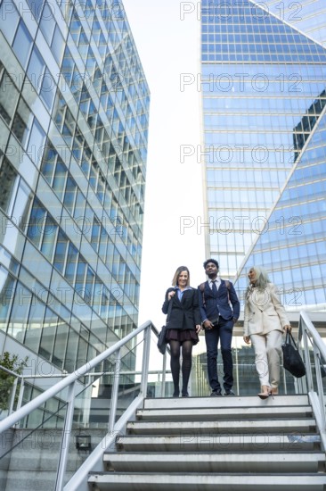 Diverse business professionals in formal attire walking down modern city stairs between glass skyscrapers, representing teamwork, ambition, and global corporate environments