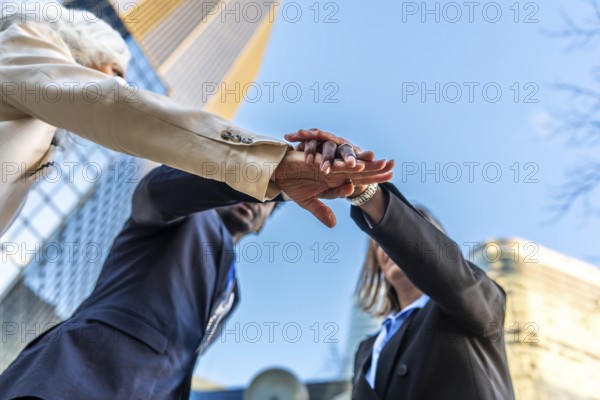 Diverse business team stacking hands outdoors in an urban setting, symbolizing unity, collaboration, partnership, agreement, and shared goals toward a common professional future