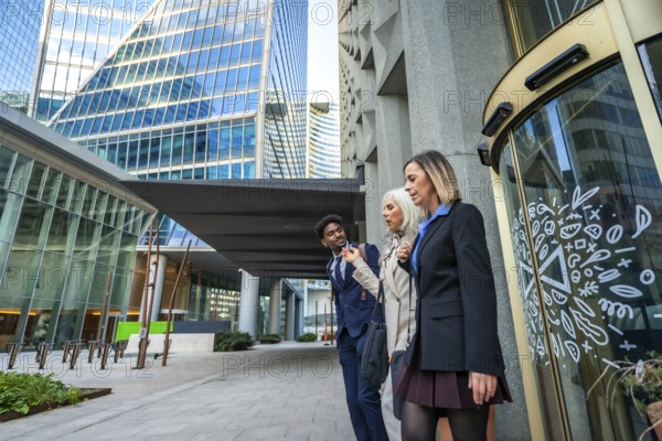 Diverse business colleagues walking and talking together, sharing ideas while navigating a modern city environment with contemporary office buildings and a revolving door