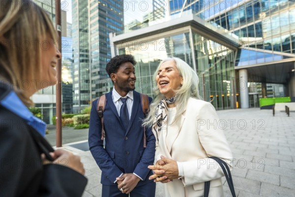 Diverse group of business people collaborating and laughing together during an outdoor meeting on a sunny day in the vibrant urban district, showcasing teamwork and positive interaction