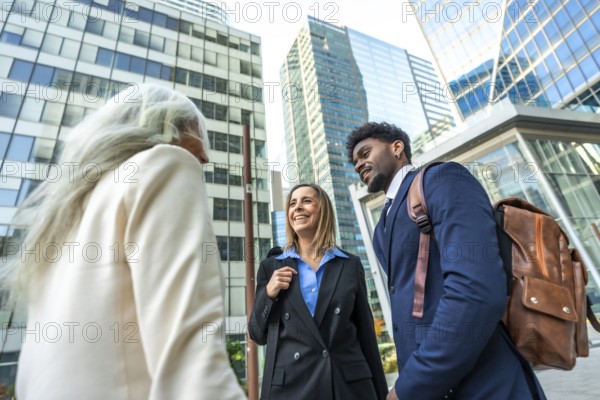 Diverse business professionals in smart casual attire chat and walk outside in a modern financial district, showcasing teamwork, collaboration and confident urban networking energy