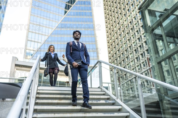 Diverse business people walking on stairs in a contemporary urban environment with tall, geometric skyscrapers, representing ambition and professional life in a bustling city