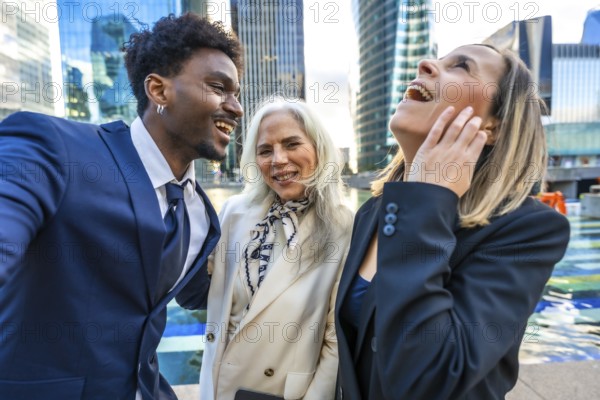 Happy business people of various ages and ethnicities are laughing together in an urban city setting with modern skyscrapers, representing teamwork, success, and positive corporate culture