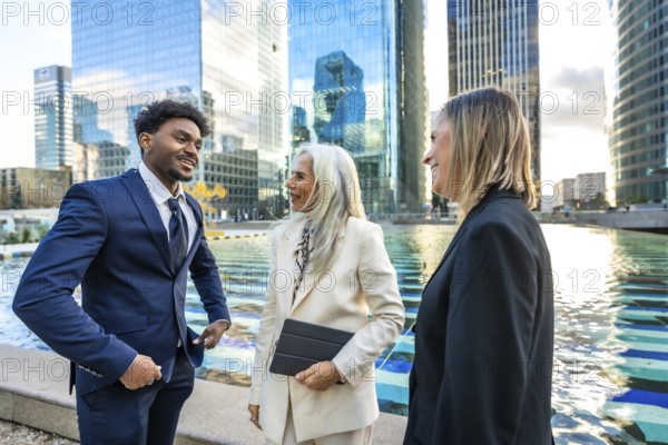 Diverse business professionals having a dynamic informal meeting and discussing ideas outdoors in a modern corporate city environment with skyscrapers reflecting in the water
