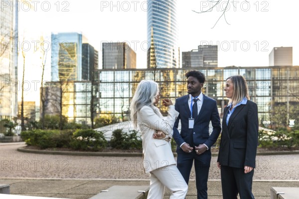 Diverse business professionals conducting an informal meeting and discussing ideas while standing together in an urban financial district with modern skyscrapers reflecting sunlight