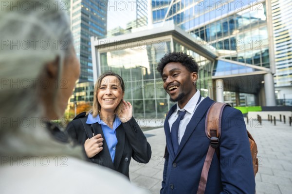 Diverse business professionals smiling and communicating while standing in a modern urban district, capturing themes of teamwork, success, and multicultural collaboration