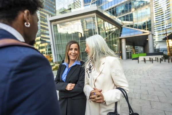 Group of multi ethnic business people engaged in an outdoor conversation with smiling women, fostering connection and collaboration against a modern city backdrop