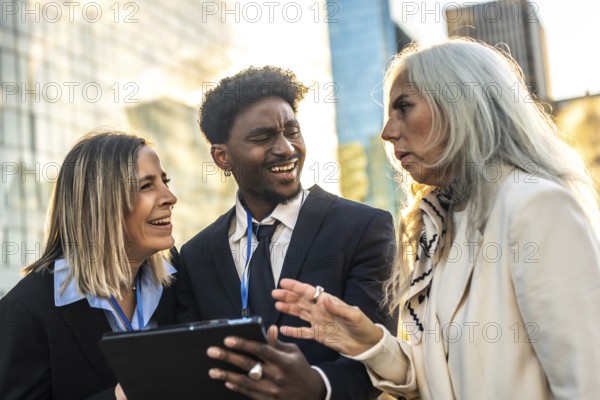 Diverse business professionals meet outdoors in the city, smiling and collaborating over a tablet as they discuss strategy, teamwork and modern workplace communication