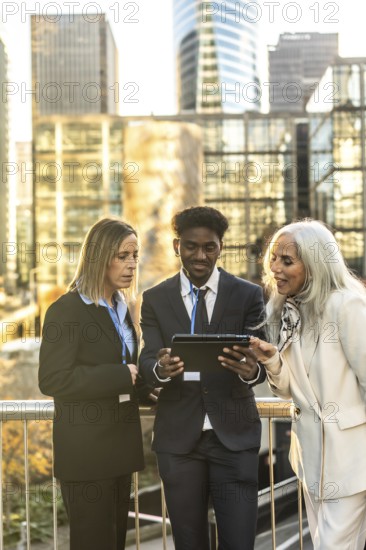 Three business colleagues from different generations and ethnicities reviewing data on a digital tablet, standing outdoors in a modern city setting, collaborating on a challenging project