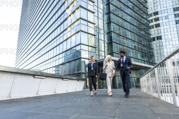 Business professionals of different ages and ethnicities are walking together, smiling, and having a discussion while leaving an urban corporate skyscraper