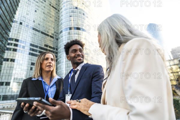 Diverse business professionals discussing projects and ideas during an outdoor meeting in a modern financial district, reflecting concepts of teamwork, strategy, and global business