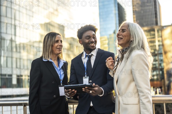 Diverse business professionals reviewing information on a digital tablet, fostering teamwork and collaboration during an outdoor city meeting in a modern urban environment