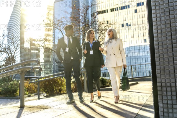 Group of diverse business people walking outdoors in a modern city during daytime, discussing strategy and collaborating on a new project while moving forward along a sunny street