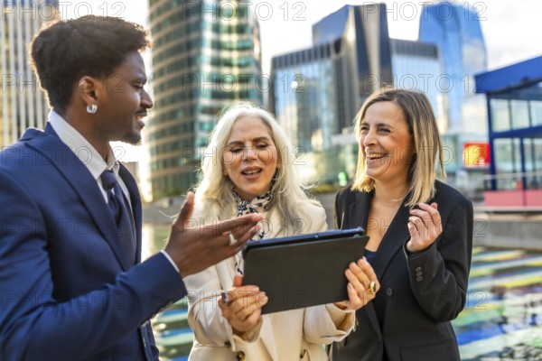 Diverse business professionals having an animated outdoor meeting, looking at a digital tablet and collaborating on a new project surrounded by a modern cityscape