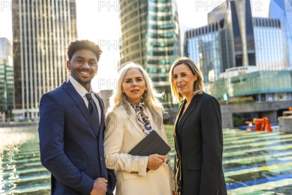 Diverse business team of professionals standing united and smiling, showcasing collaboration and success in a modern urban environment with office buildings during sunset