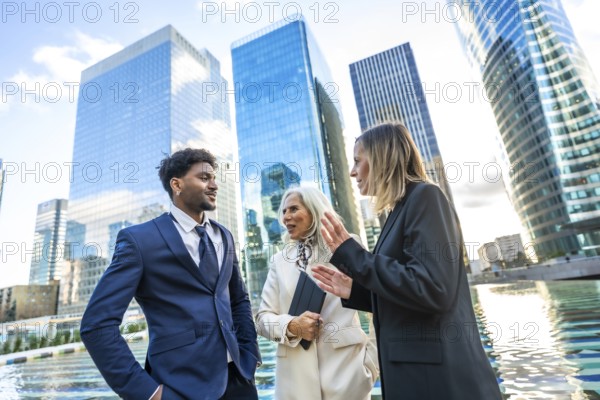 Diverse business professionals in formal attire discussing work and collaborating outdoors, reflecting teamwork and corporate success with modern city skyscrapers in the background