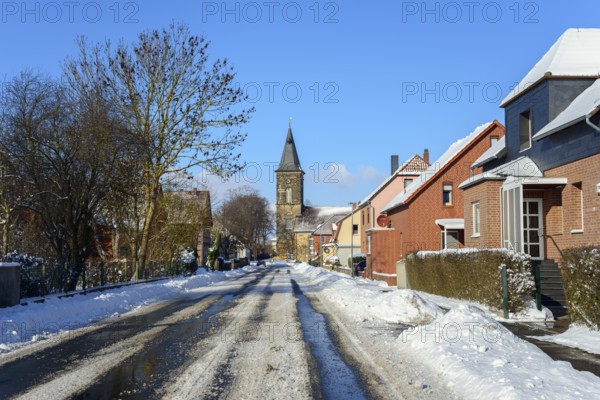 Wintery village road with snow cover, surrounded by houses and a church tower under a blue sky, Sankt Pankratii church, Groß Solschen, Ilsede, Peine district, Lower Saxony, Germany