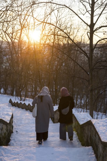 Two woman walk on snowy stairs with evening sun in Volkspark Friedrichshain on 07.01.2026