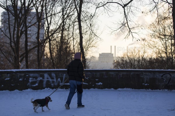 A walker with a dog runs on the Großer Bunkerberk with a view of the Berlin power plant in Volkspark Friedrichshain on 07.01.2026