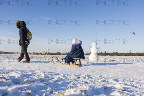 A woman drags a child on a sled past a snowman on Tempelhofer Feld in Berlin on 11.01.2026
