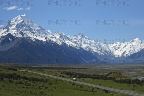Motorhome camper van drives on a lonely country road against a huge mountain backdrop with a river delta through the Hooker Valley in Aoraki National Park, Aoraki Mount Cook National Park, Canterbury, New Zealand