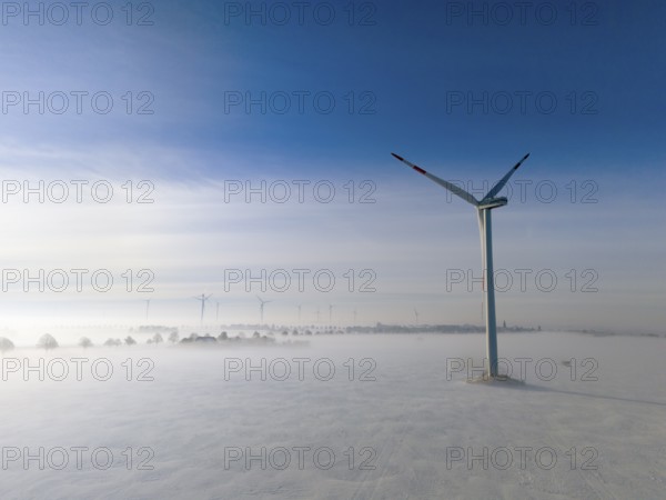 Wind turbine rises above foggy snow-covered landscape in clear blue sky, aerial view, wind turbine in snow in fog, between Bülten and Solschen, Ilsede, Peine district, Lower Saxony, Germany