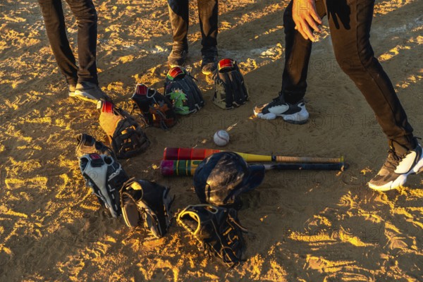 Baseball players gathering on a dusty field at sunset, discussing strategy while their bats, helmets, and gloves lie on the ground, preparing for a game