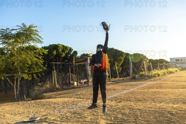 Baseball player in uniform leaps on a sunny field, arm outstretched with glove to snatch a fly ball over dusty infield during an intense outdoor game