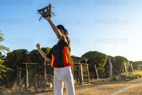 Young boy in baseball uniform and cap catches a ball with his glove on a sunny dirt field, focused in mid reach during outdoor practice or a casual game in summer daylight