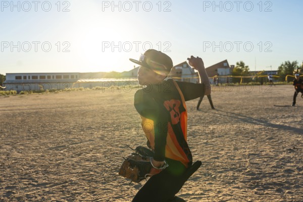 Young baseball player wearing a cap and jersey, preparing to throw the ball during a game on a dusty field at sunset, focusing on the pitch while practicing