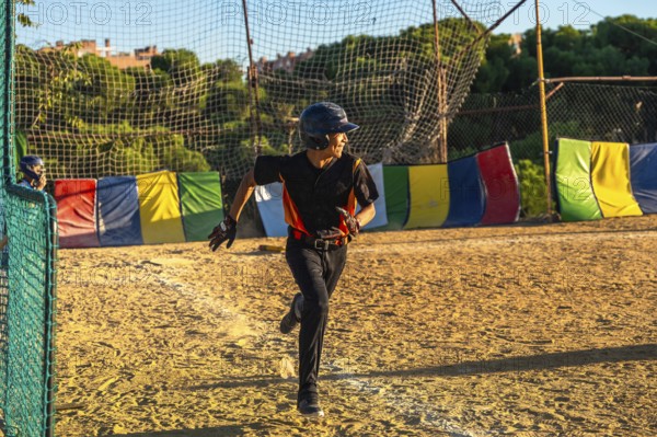 Young baseball player, wearing a helmet and uniform, running with determination on the dirt field during a daytime game, displaying action and competitive spirit