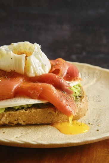 A breakfast dish features sliced smoked salmon and a poached egg on top of toasted bread. Liquid egg yolk runs down the fish onto the plate